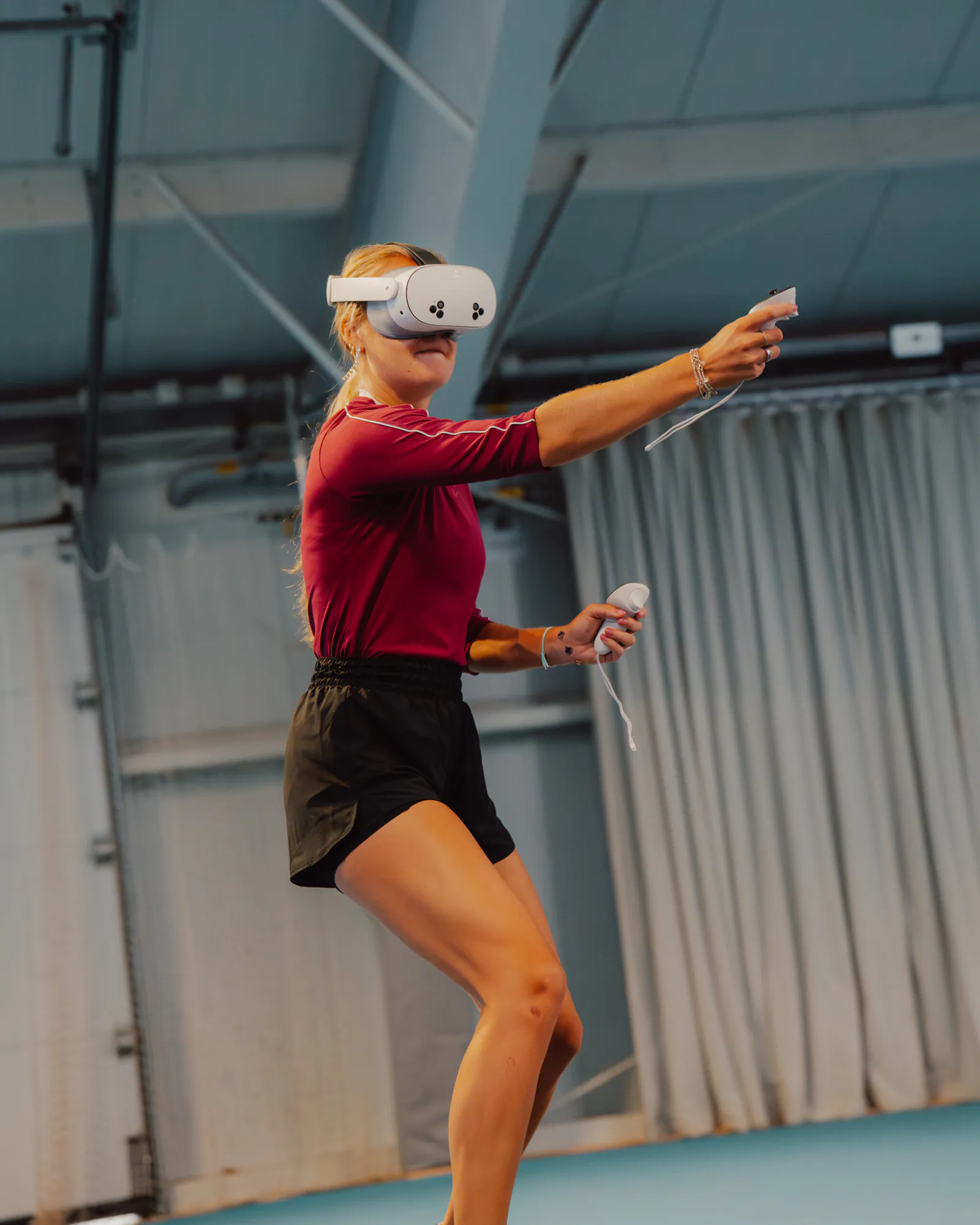 Sportlerin in Bewegung mit VR-Headset und Controllern in einer Sporthalle